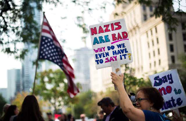 A woman carries a sign at a protest that reads Nazis are bad, why do we even have to say it?