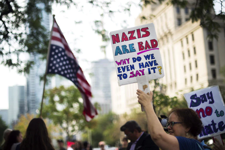 A woman carries a sign at a protest that reads Nazis are bad, why do we even have to say it?