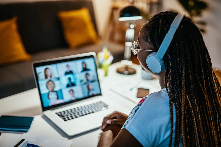 Woman wearing glasses and headphones sits at a desk in front of a laptop screen