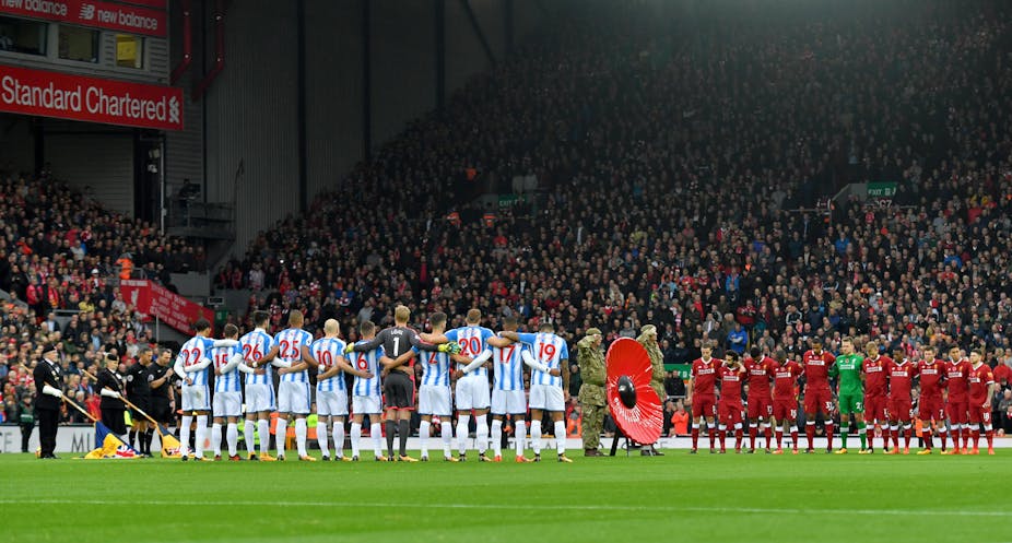 Players from two football teams link arms on the pitch as a giant poppy is displayed by members of the armed forces.