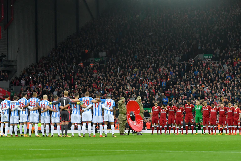 Players from two football teams link arms on the pitch as a giant poppy is displayed by members of the armed forces.