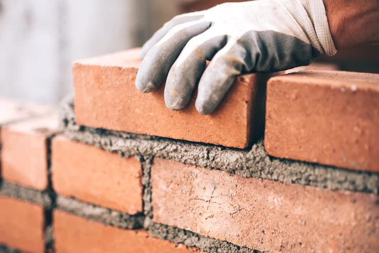 A gloved hand lays a brick in a wall.