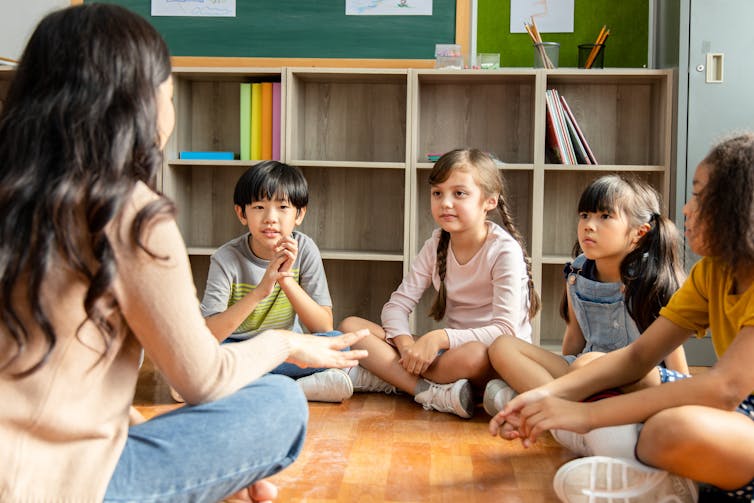 A teacher sits with kids as they engage in conversation. There are four kids.