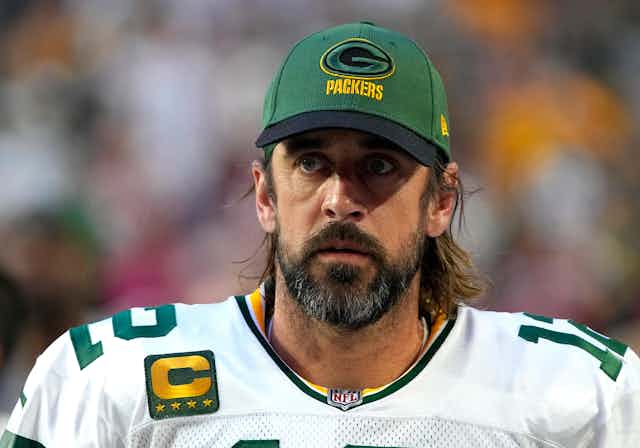Head and shoulders shot of NFL quarterback Aaron Rodgers in his Green Bay Packers uniform and a team hat.