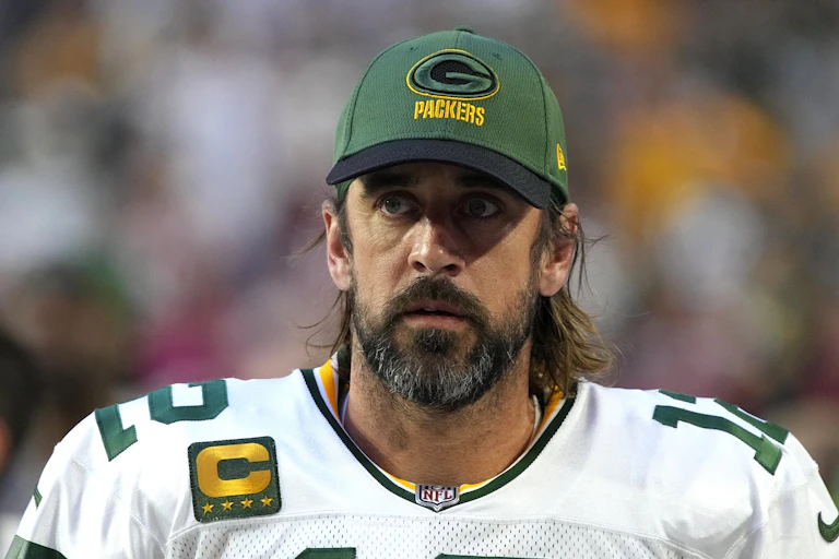Head and shoulders shot of NFL quarterback Aaron Rodgers in his Green Bay Packers uniform and a team hat.