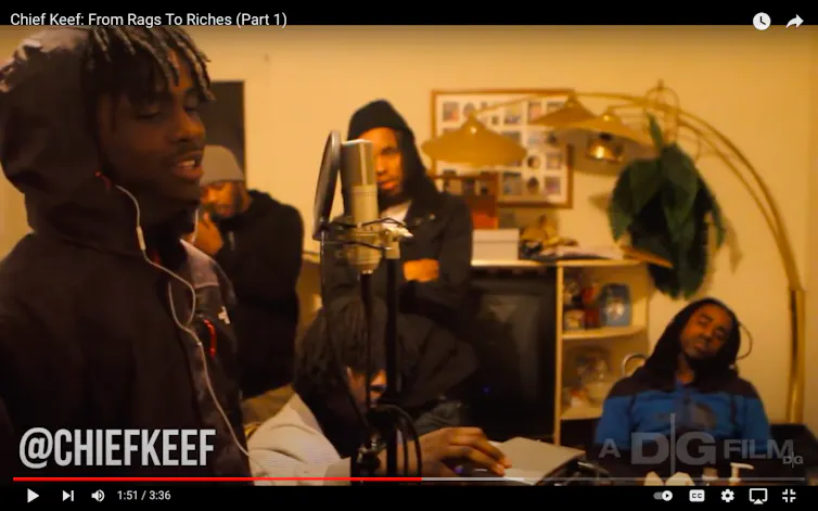 Man raps into microphone in front of a few friends.