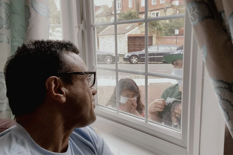 A man looks out a window at two people wearing masks