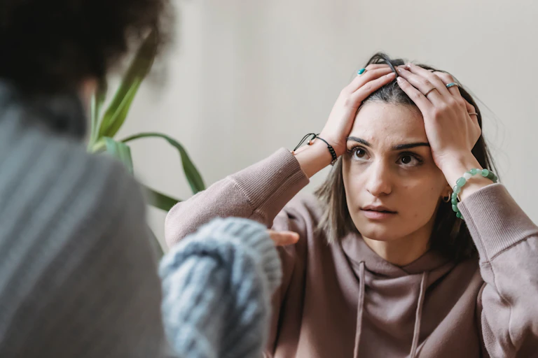 A woman looks at another women with her hands on her head.