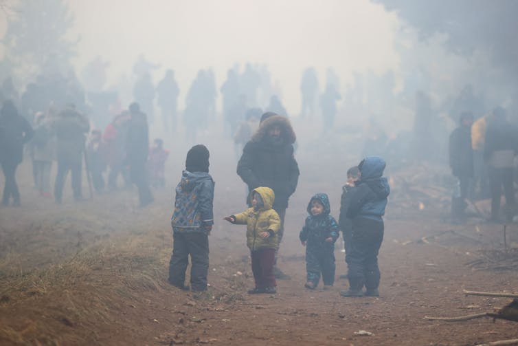 A group of migrants wearing cold weather clothing at the Poland/Belarus border including several children.
