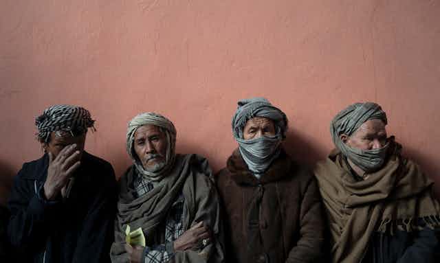 Four men in scarves huddle together in a line.