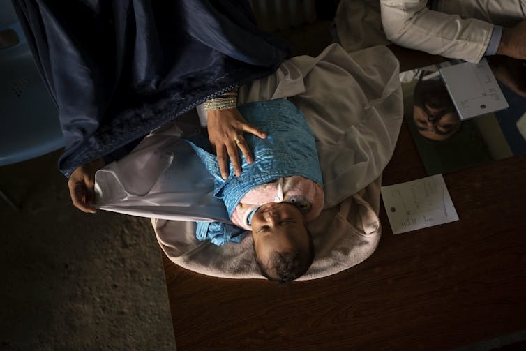 A baby swaddled in a blue blanket lies on a desk.