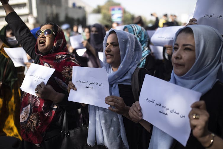 Afghan women in head scarves carry signs and chant during a protest