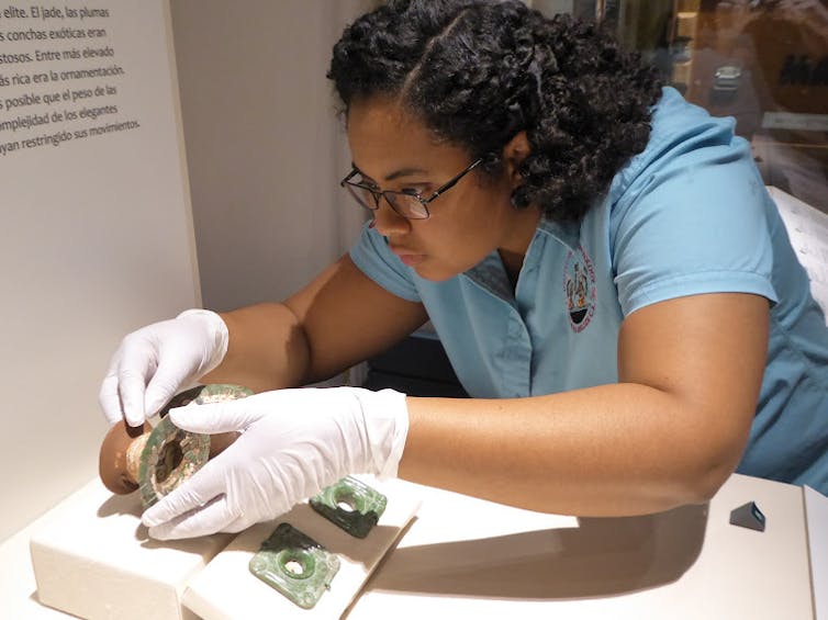 A woman wears gloves as she carefully arranges a small artifact