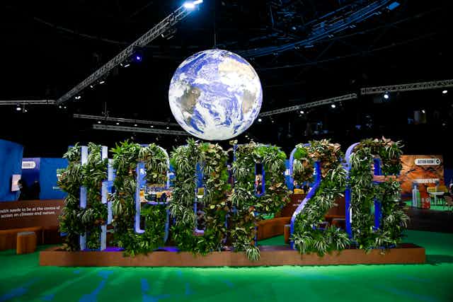 A sign filled with plants spelling out '#COP26' under a globe.