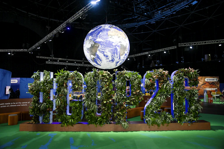 A sign filled with plants spelling out '#COP26' under a globe.