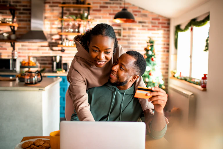 young couple looking at a laptop with christmas decorations in background