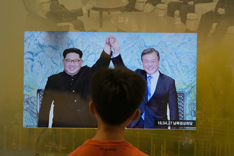 A boy facing away looks at a video monitor displaying two men facing forward holding each other's hand raised above their heads