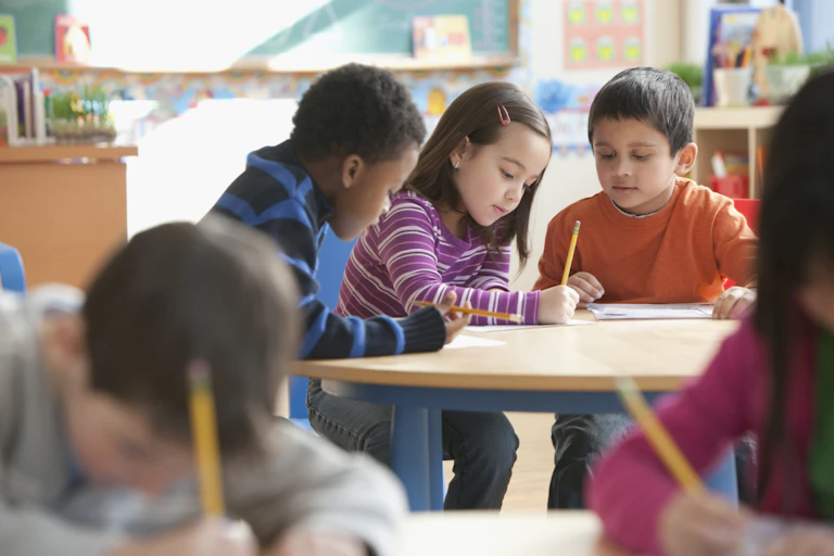 Three young students work together at a desk in school classroom