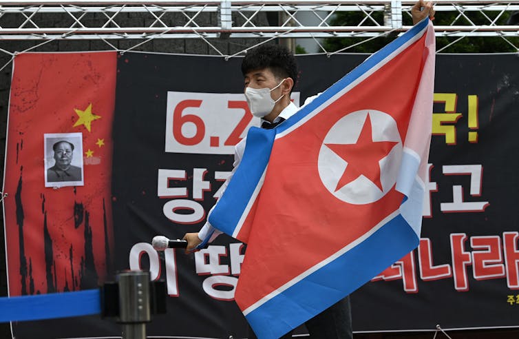 A man standing on a stage while holding a microphone tears a flag