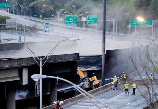 Workers in yellow vests survey a section of an overpass that collapsed after a large fire in Atlanta