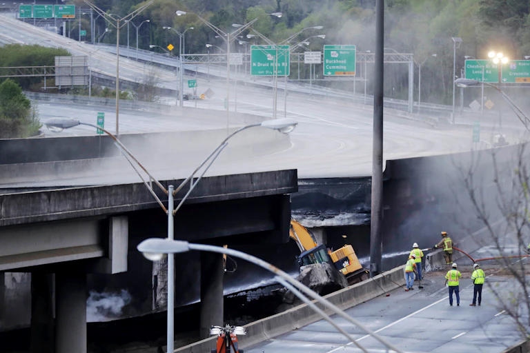 Workers in yellow vests survey a section of an overpass that collapsed after a large fire in Atlanta
