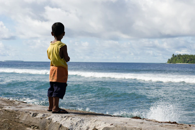 A boy stands on a sea wall on a tropical island overlooking the tide.