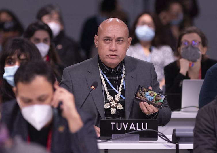 A Tuvalu delegate at the UN climate negotiations holds up a photo of his grandchildren on his phone.