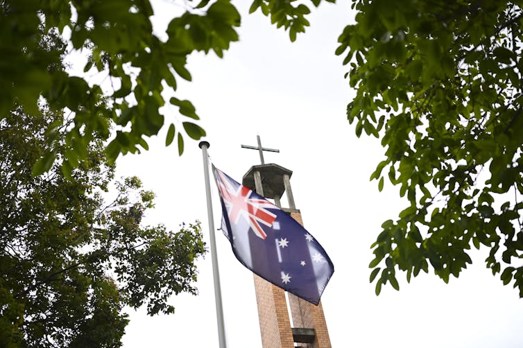 An Australian flag flies in front of a church steeple.
