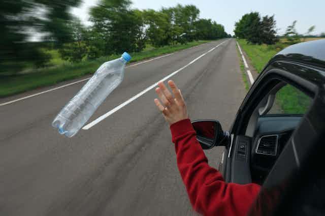 Una persona arroja una botella de plástico desde un coche.