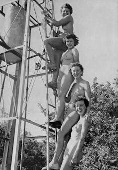Four nude women stand on a ladder, smiling at the camera