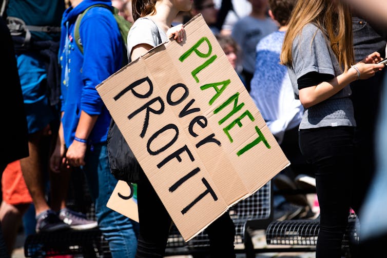 Woman at protest holds sign reading 'Planet over Profit'