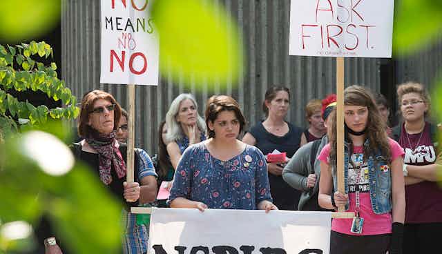 Students stand wih signs at a rally that say 'no means no' and 'ask first.'