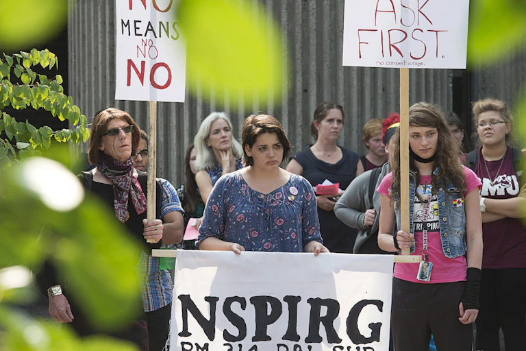 Students stand wih signs at a rally that say 'no means no' and 'ask first.'