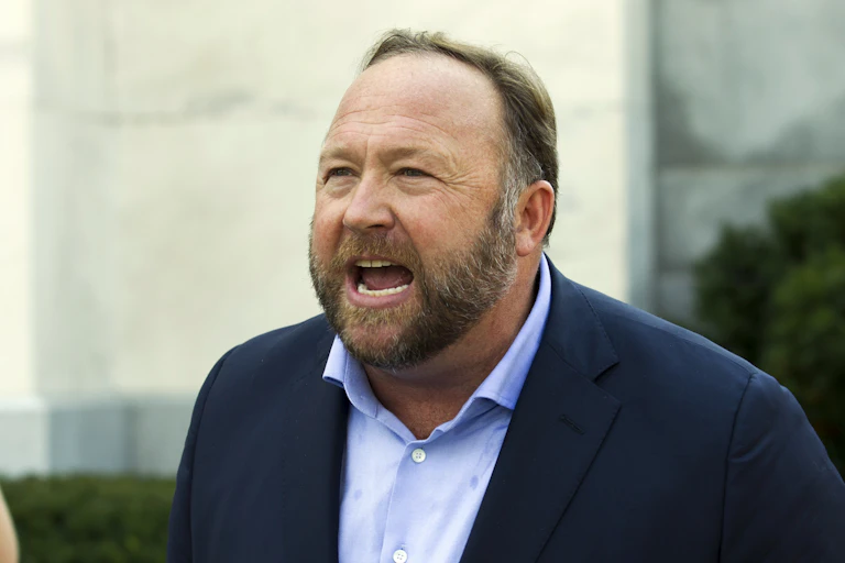 A bearded Alex Jones in a blue blazer and light blue shirt, looking like he's angry.