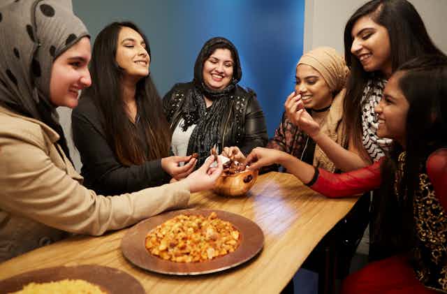 Six girls sitting around a table, sharing food as they break fast during the month of Ramadan