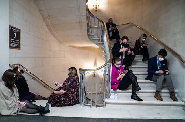 Reporters sit on the steps inside a Congressional building.