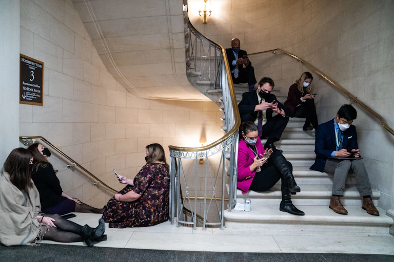 Reporters sit on the steps inside a Congressional building.