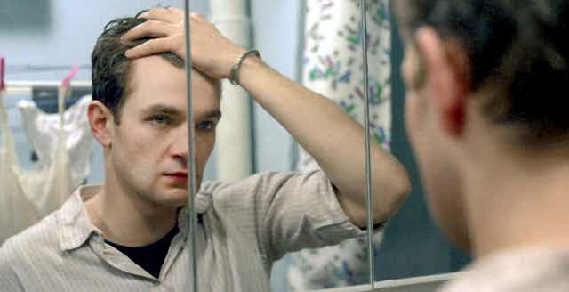 A man looks into a mirror and holds his hair back.