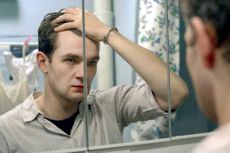 A man looks into a mirror and holds his hair back.