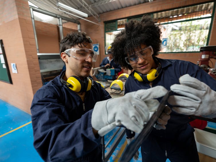 Two male college-age students wear protective goggles, earphones and gloves.