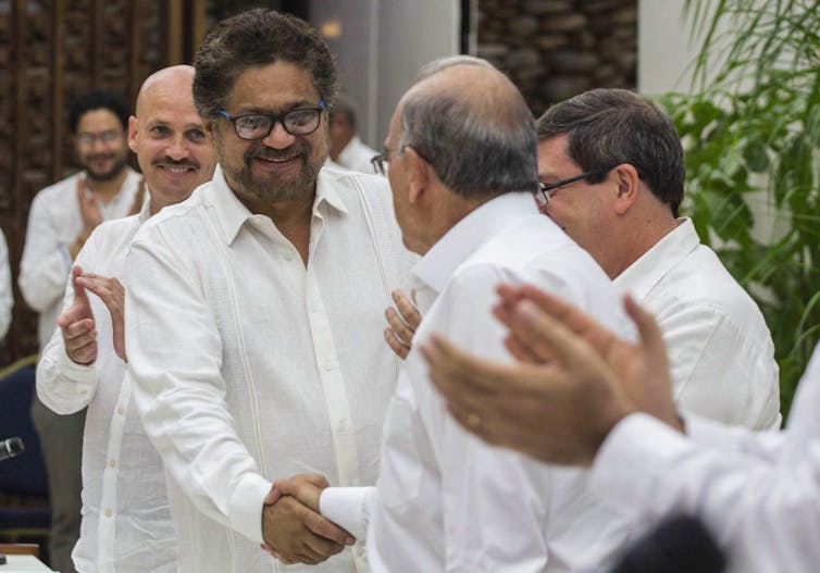 Men wearing white applaud and shake hands.