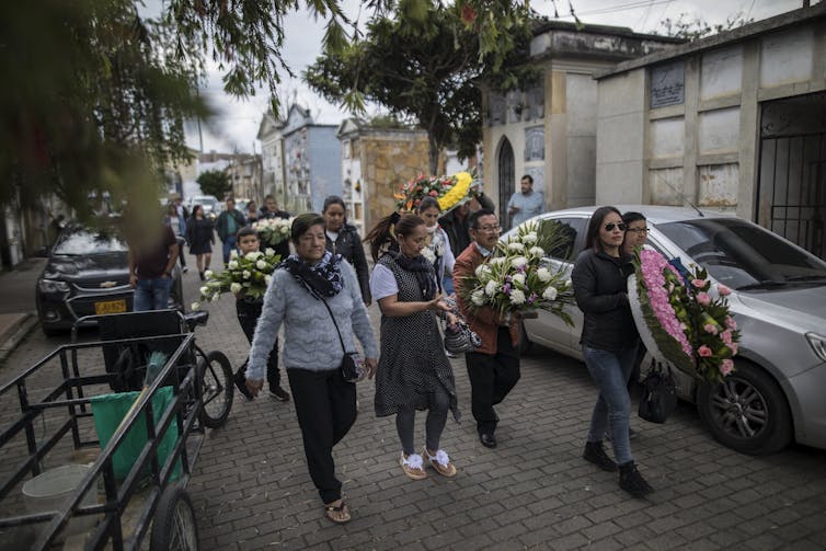 A group of women walk down the street carrying flowers.