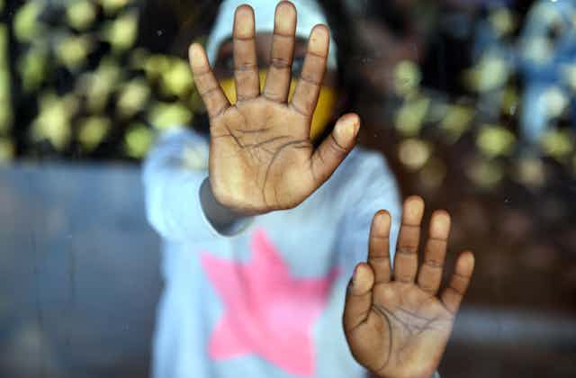 An Aboriginal child presses their hands up against a window.