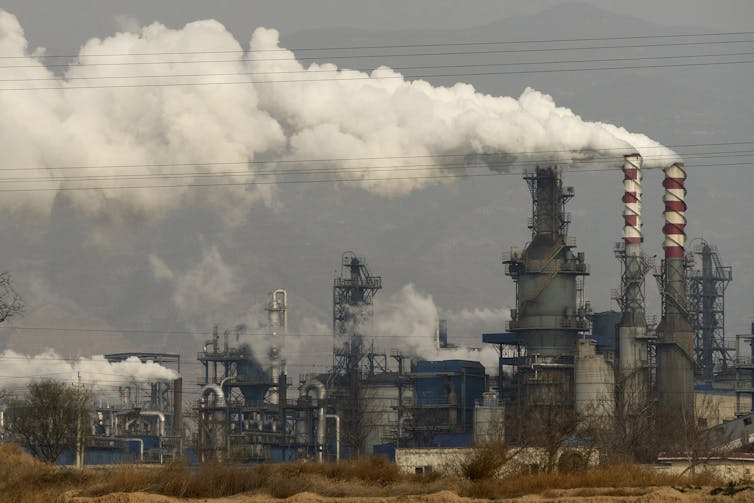 Thick white smoke and steam billow from stacks against a grey sky.