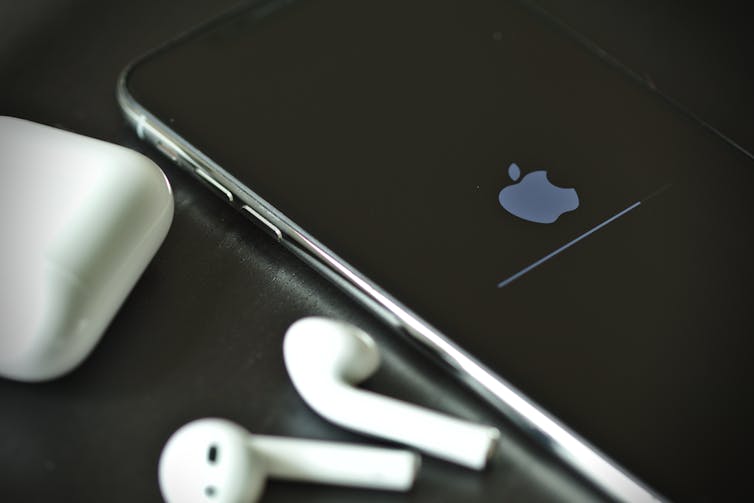 An iPhone and airpods on a dark surface