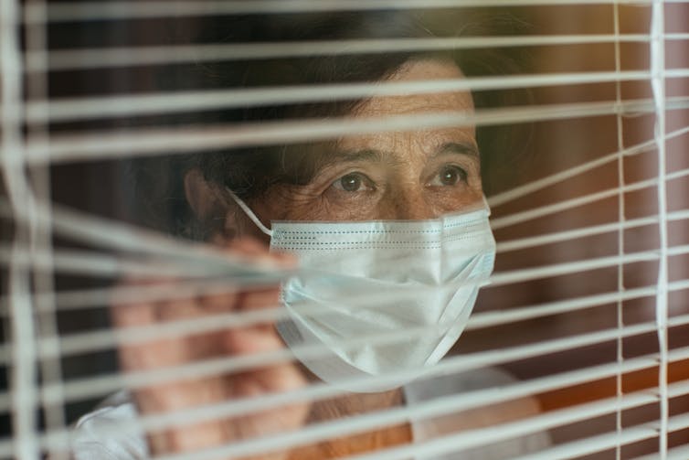 Older woman in facemask looking through a window