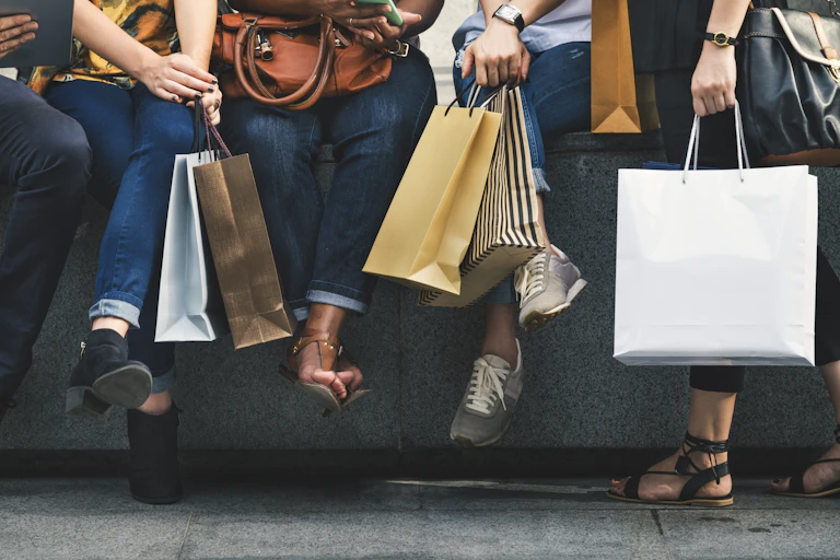 Five people picture from the waist down sitting along a cement wall with many shopping bags