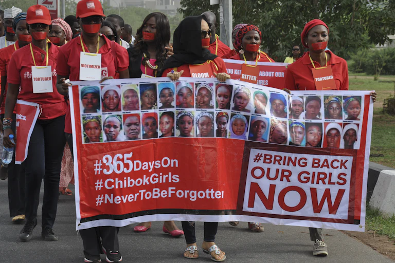 A group of women, with their mouths covered to symbolise absence of free speech, march carrying a banner showing the photos of some of the girls kidnapped by Boko Haramin Nigeria