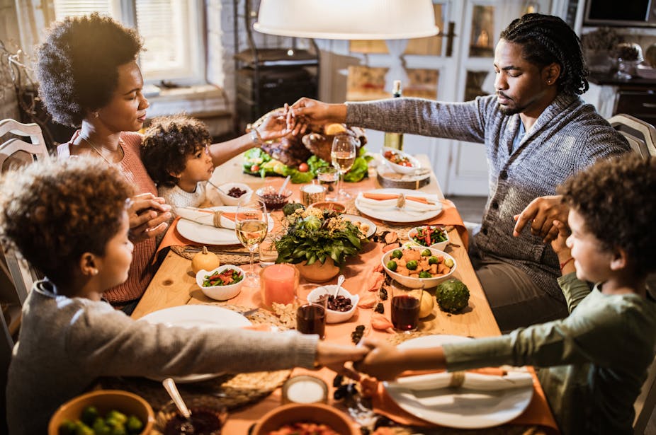African American family holding hands and praying before their Thanksgiving meal at home.