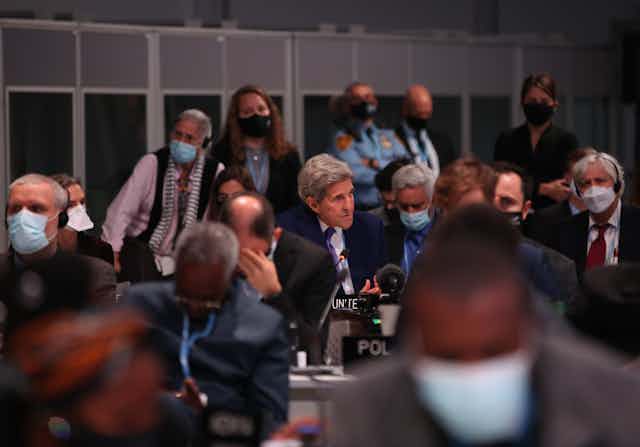 John Kerry speaking a the conference surrounded by people